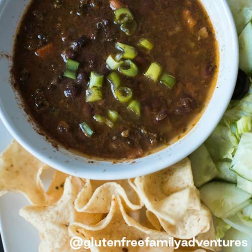 Beans & Greens Soup in white bowl with a side of tortilla chips and lettuce on a white plate.