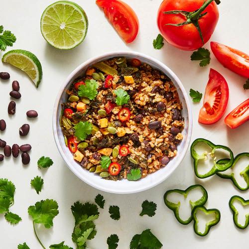 Brown Rice Taco Bowl with ingredients surrounding it: Limes, Tomatoes, Peppers, Beans, and Cilantro