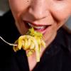 A close-up of Creamy Butternut Squash Noodles twisted on a fork near a woman's mouth.