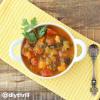 White bowl of Butternut Squash Ratatouille Soup with silver spoon on a yellow linen and wooden table. 