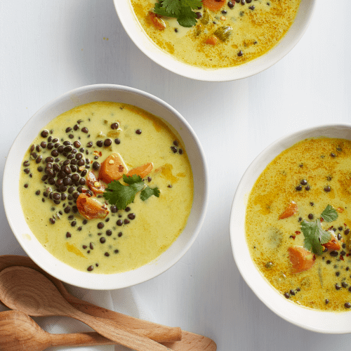 Carrot Lentil Curry Soup SOUP ON WHITE BACKGROUND WITH THREE WOODEN SPOONS.