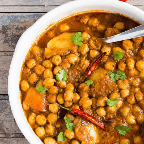 Channa Potato in a white bowl on a gray background with spoon. 