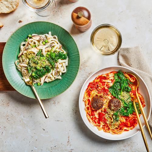 Creamy Spinach & Mushroom Noodles and Vegan Meatballs & Marinara Noodles on a table with utensils.