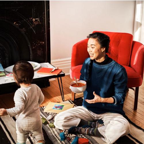 Woman and baby in living room with red chair and fire place eating Black Eyed Pea & Tomato Stew.