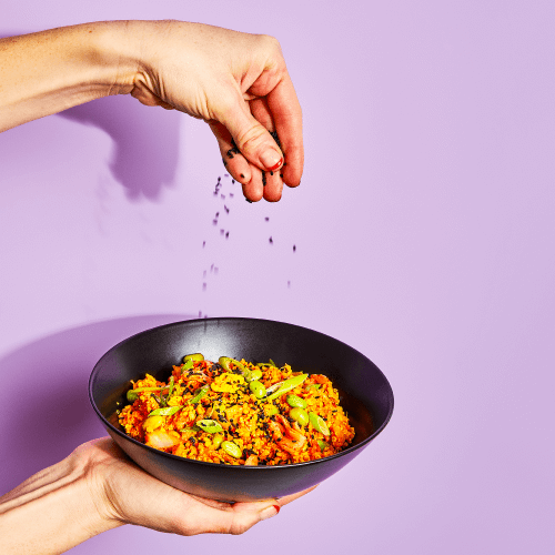 Kimchi Bowl being held up and sprinkled with sesame seeds.