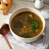 Big white pot of lentil kale soup with copper ladle on a gray linen cloth. 