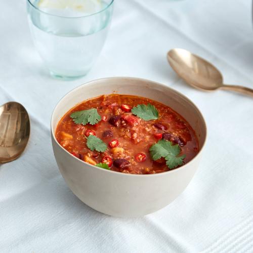 White bowl of mexican tomato with two gold spoons, a glass of water on a white table cloth.