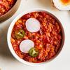 Overhead shot of Tomato Quinoa Chili Soup in a white bowl with radishes and jalepeno garnish on a white background.