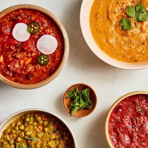 Tan bowl of Tomato Quinoa Chili Soup, pink bowl of Cumin Sweet Potato Puree Soup, tan bowl of Red Beet Quinoa Grain Bowl, beige bowl of Green Split Pea Soup, small wooden bowl of mint on a white background.