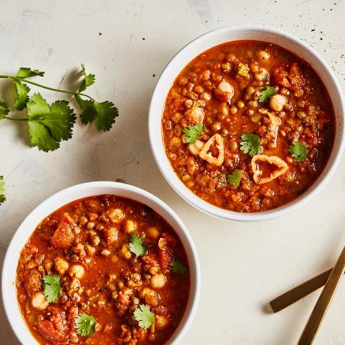 Two white bowls of Spiced Lentil & Chickpea Stew Soup Stew with cilantro on a white background.