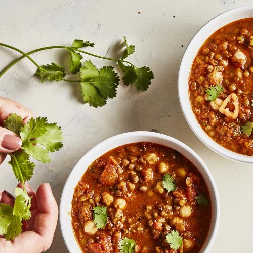 Person adding cilantro to bowls of Spiced Lentil and Chickpea Stew