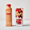 Strawberry Goji in Bottle with cup of strawberries, coconut meat, goji berries, cashews, and cinnamon sticks. Sitting up right on a white background. 