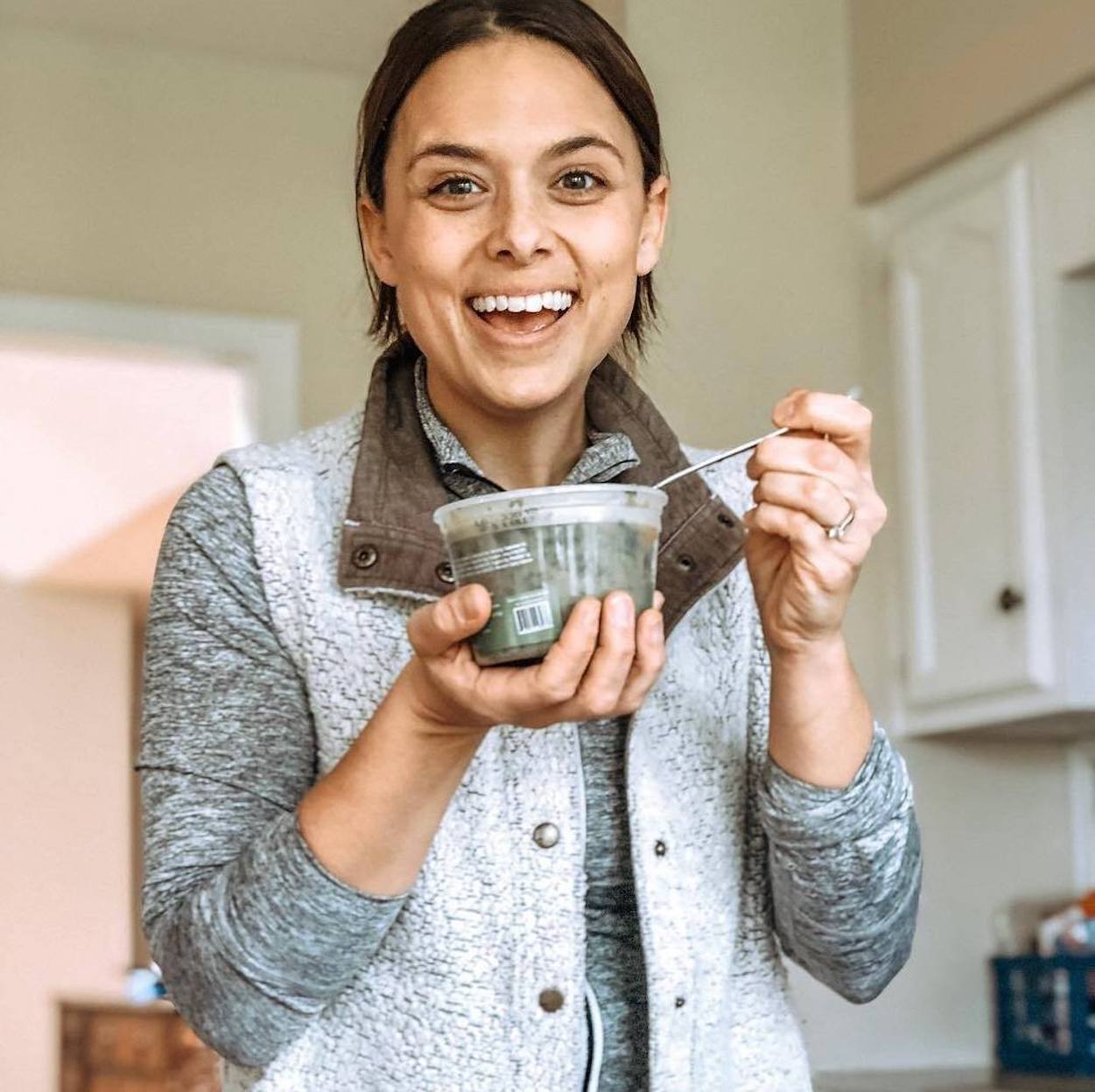 A woman with a broad, wide-eyed grin holds a Splendid Spoon bowl in front of her.